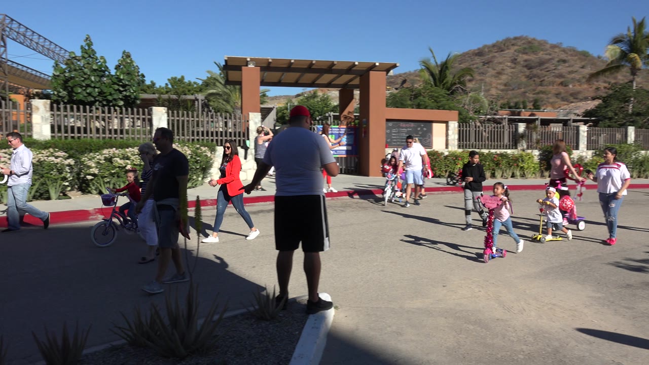 Families pass along a curb with children on scooters and bikes.