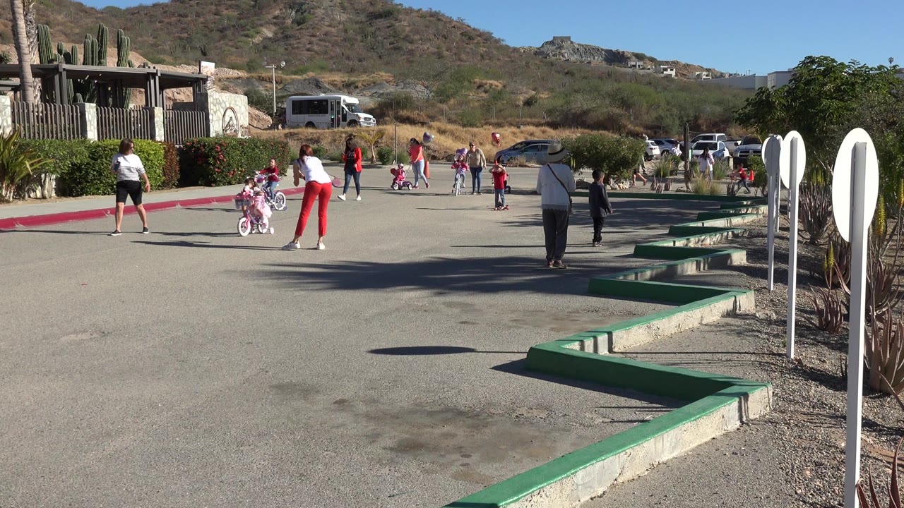 Children and adults on a paved outdoor area with bikes and scooters.