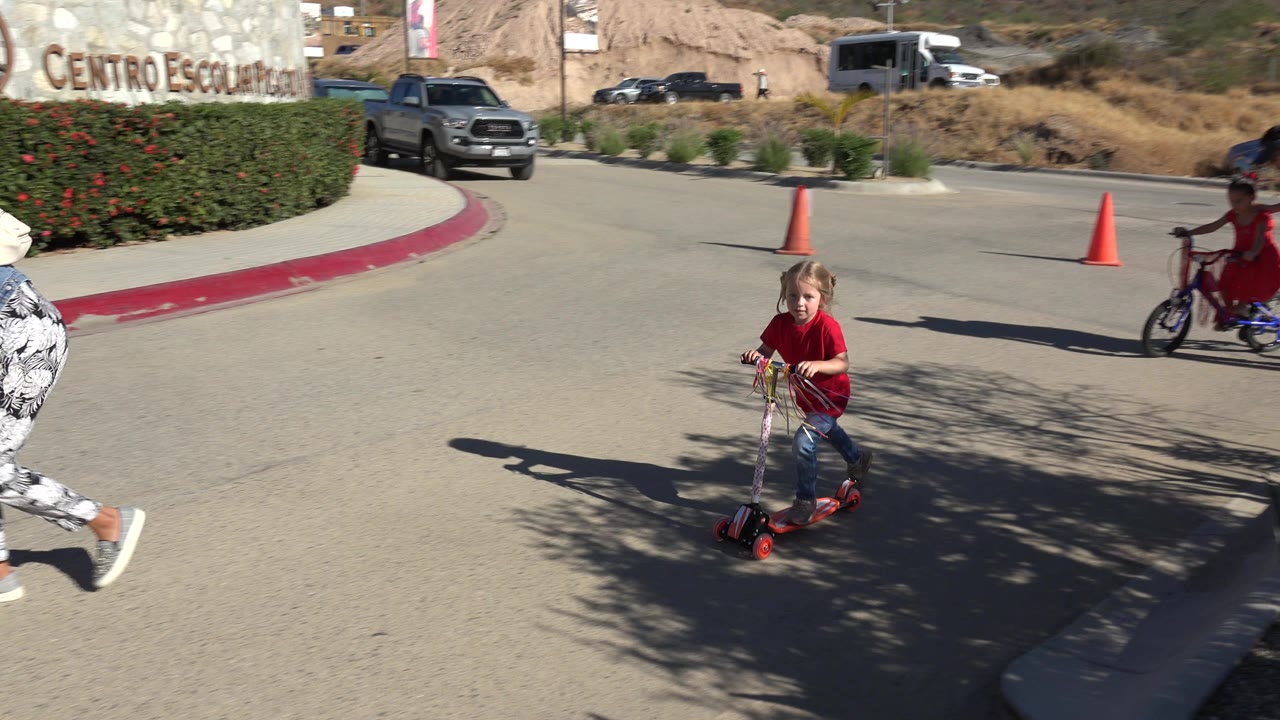 Child on scooter near pedestrians on a sunny street.