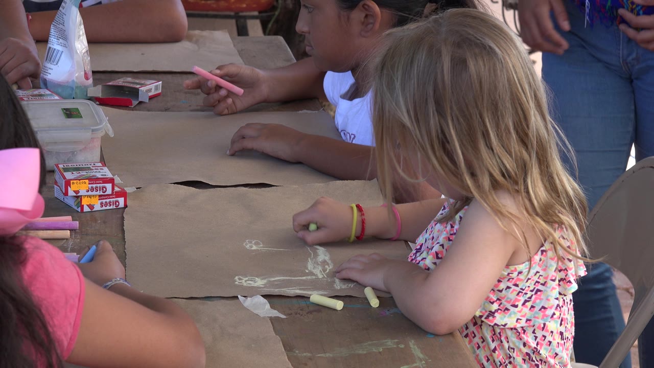 Children in Los Cabos, Mexico work around the drawing table while an adult stands beside them and chalk pieces rest on the paper.