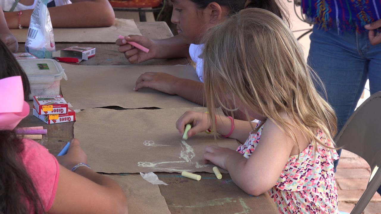 Blonde child draws while children sit around the table.