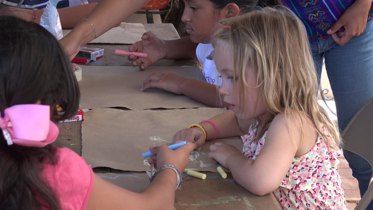 Children drawing with chalk on brown paper at a table.