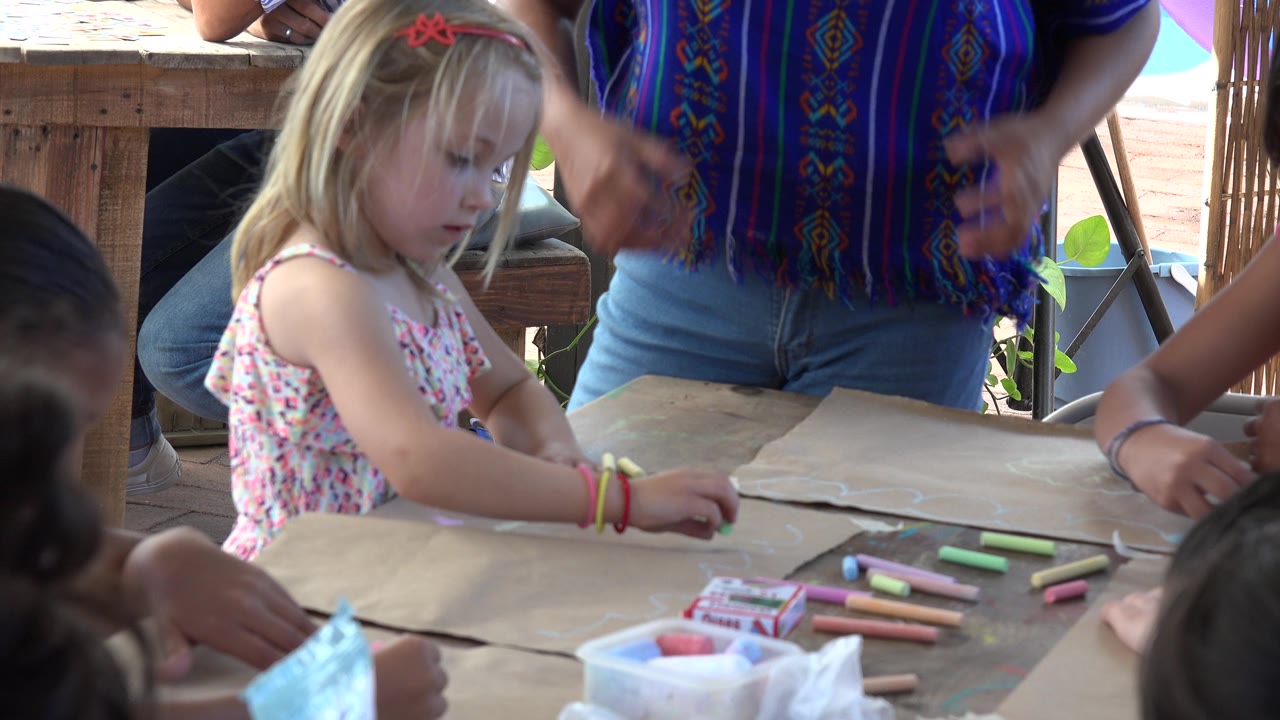 In Los Cabos, Mexico, the child looks down at the table while chalk pieces lie nearby and the instructor stands close with hands raised in explanation.