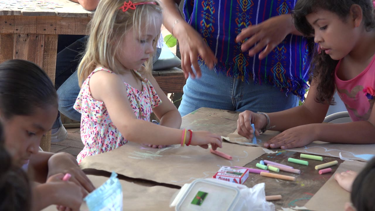 Children draw at a wooden table while an adult guides them.
