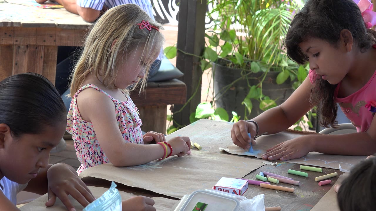 Children drawing with colored pencils at a wooden table.