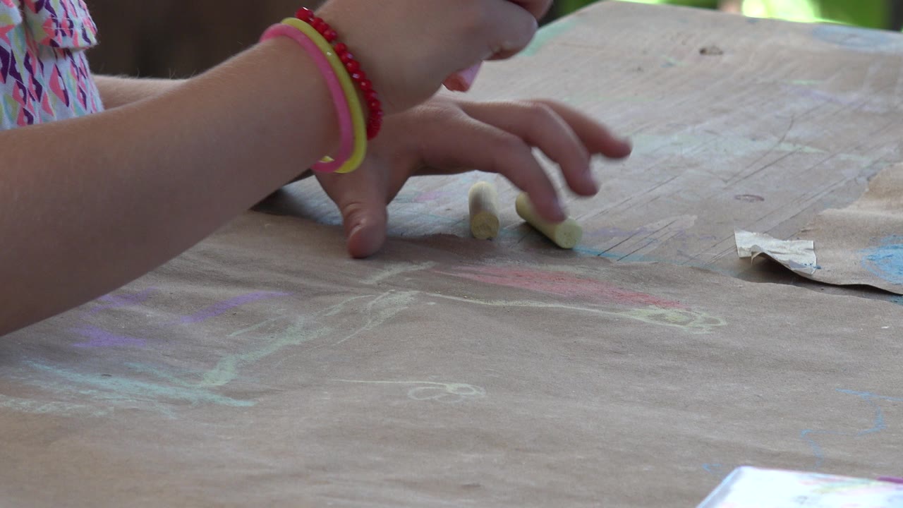 Child's hands above brown paper with chalk on a table.