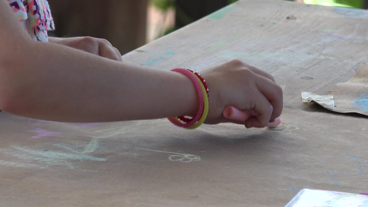 Child's bracelet-wearing arm over a chalk-marked table.