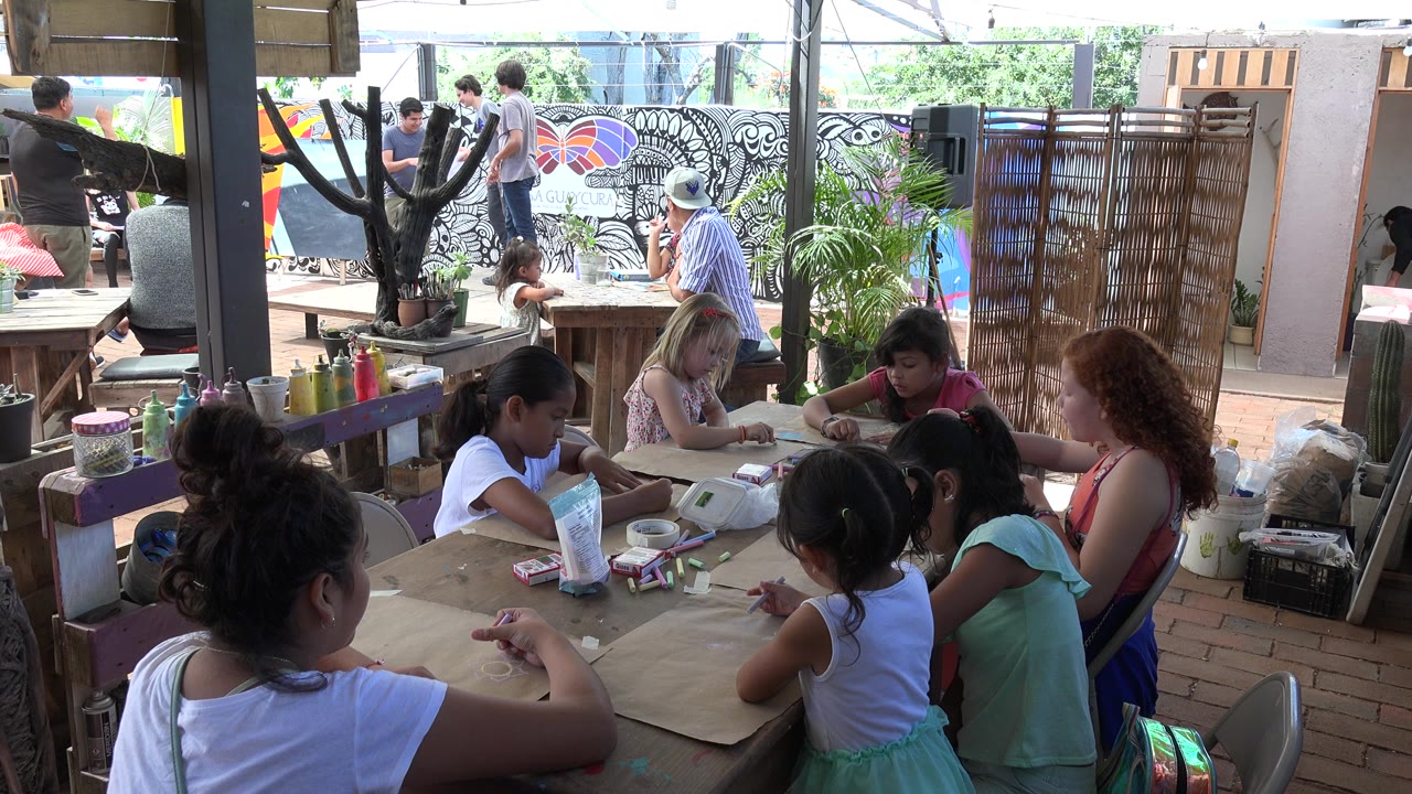 Children and adults gathered around tables in a covered outdoor activity space.