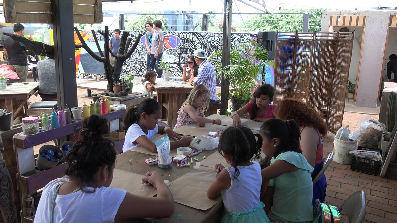 Children and adults around a craft table under a shaded patio.