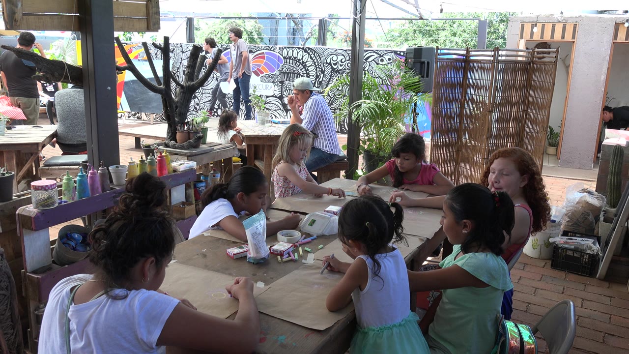 Girls seated around a paper-covered activity table in a shaded workspace.