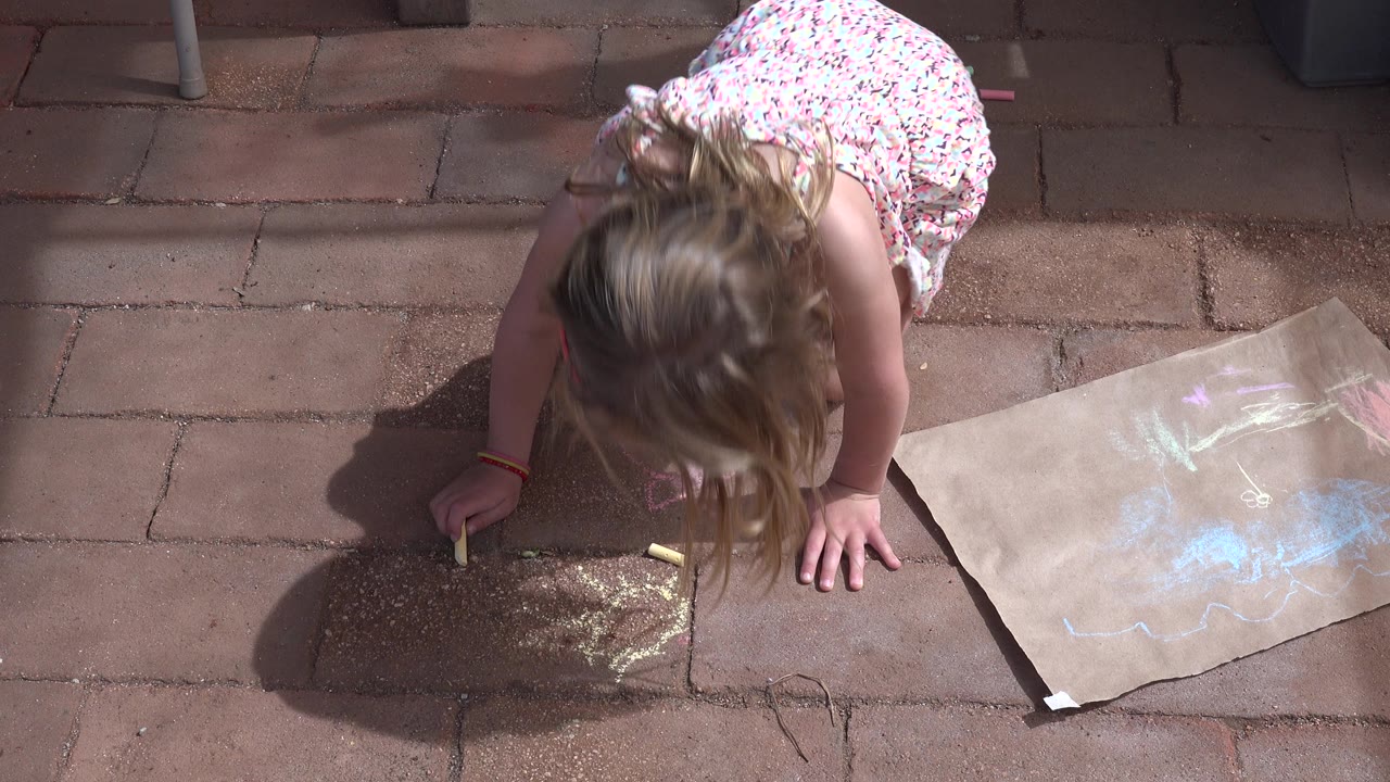 Overhead view of girl leaning over chalk art on patio.