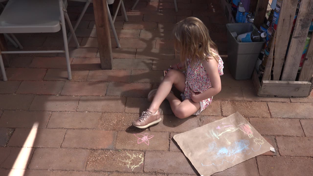 Young child sitting on patio pavers near chalk drawings.