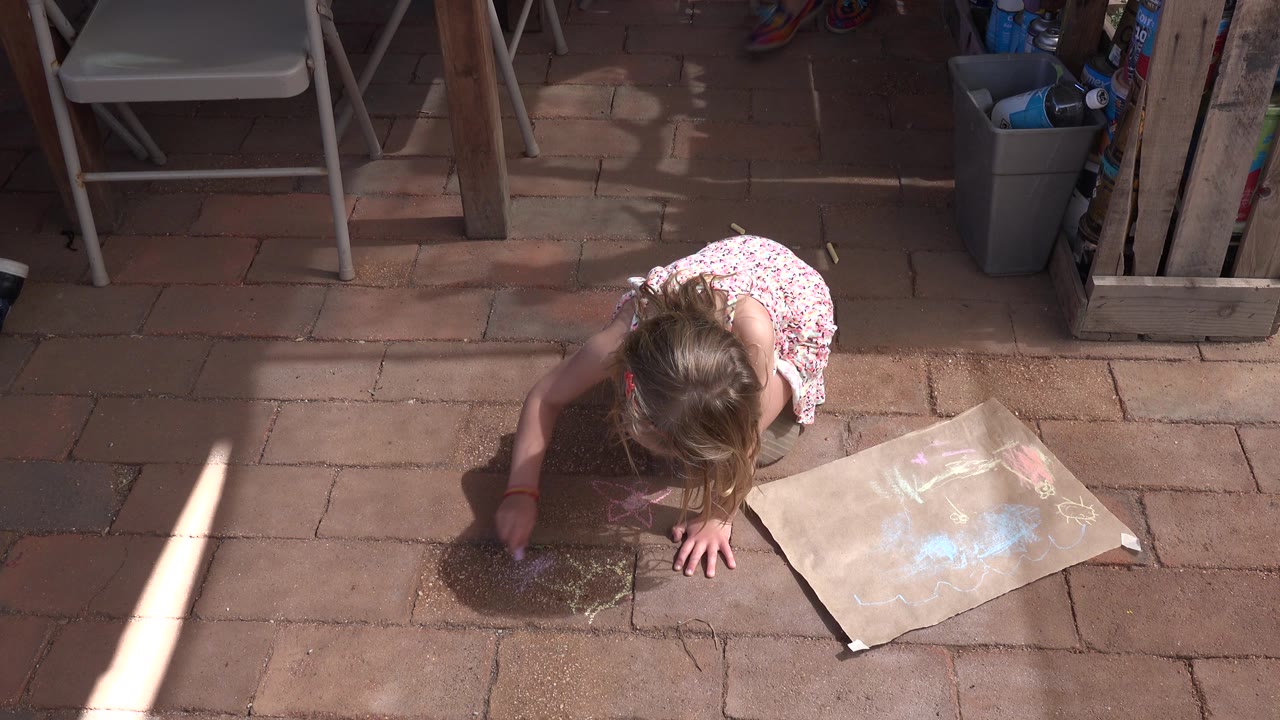 Child crouched over chalk drawing with paper beside her.