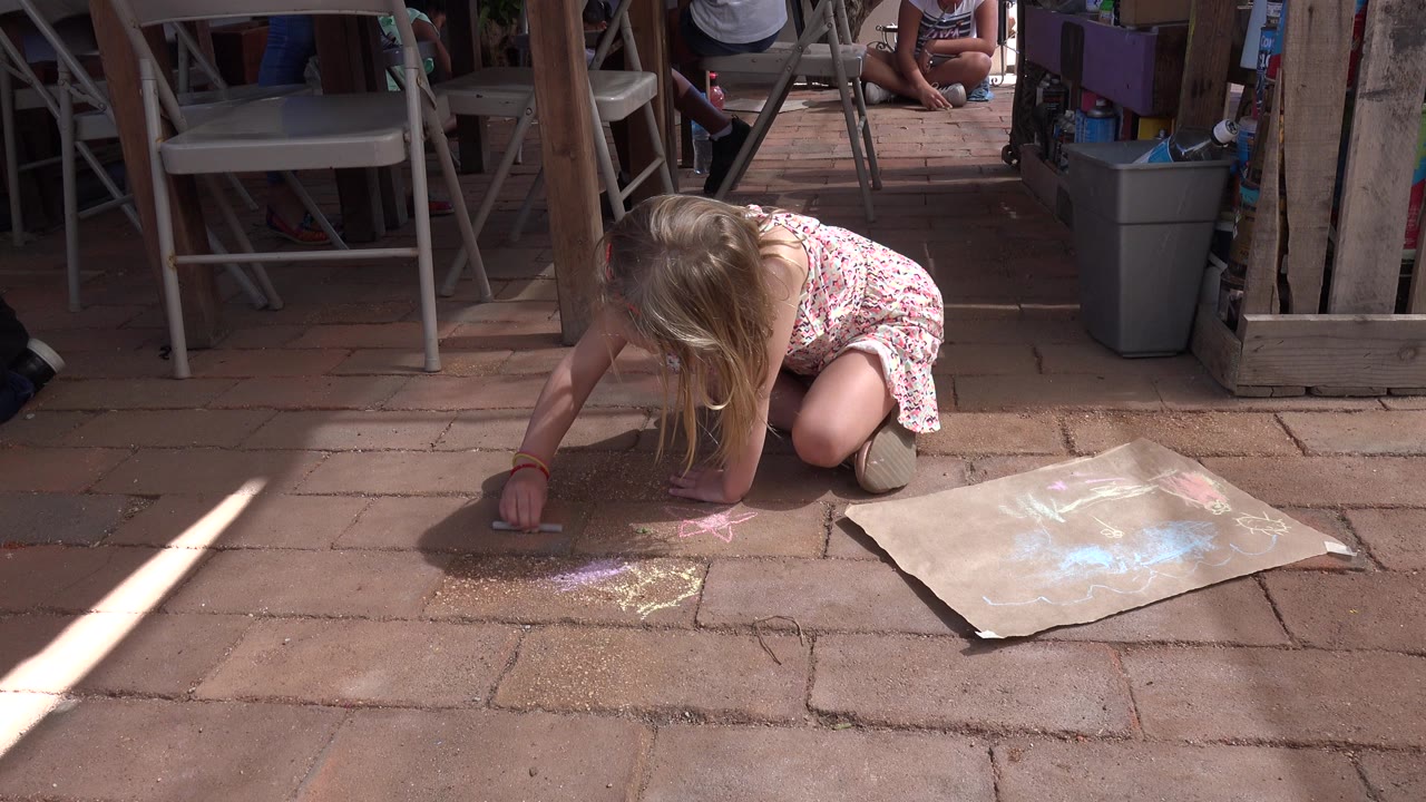 Young girl kneeling on paving stones with sidewalk chalk