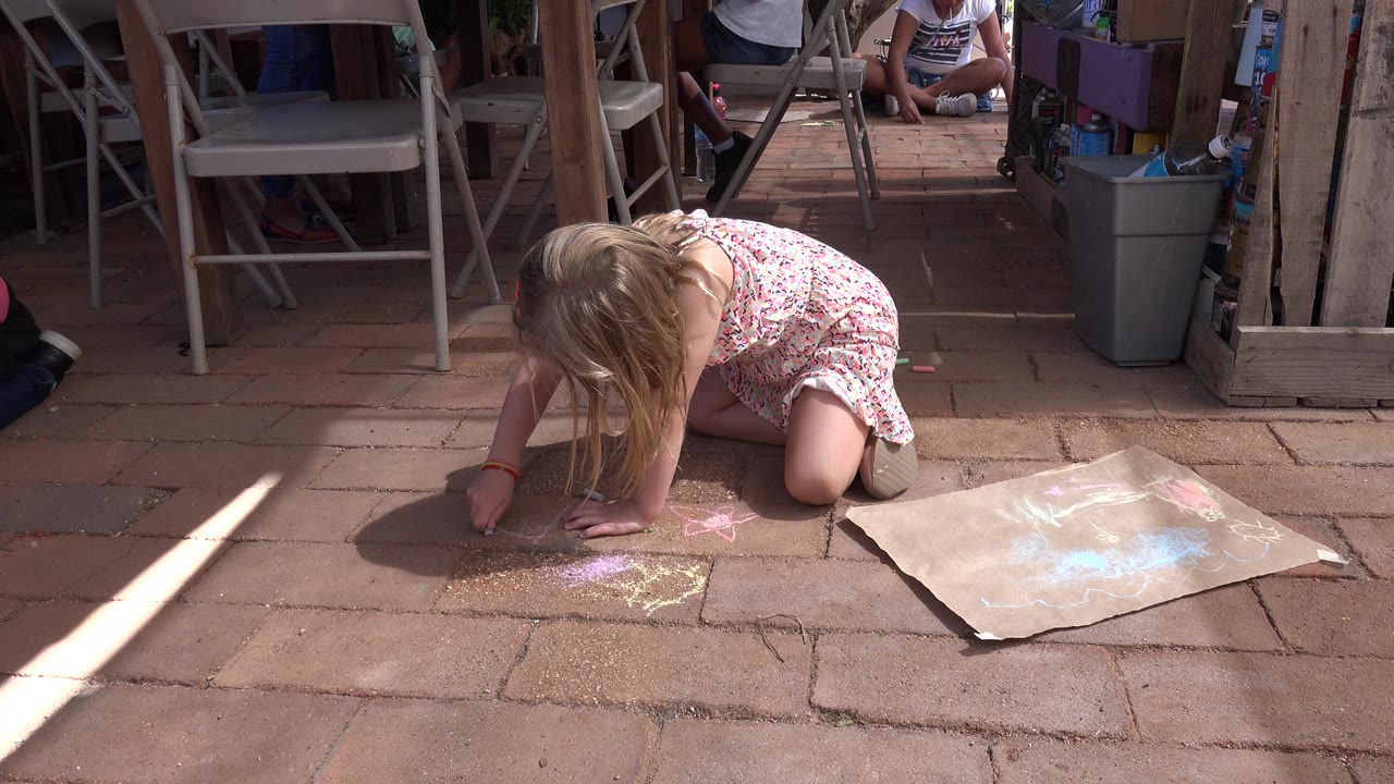 Child draws with chalk beside a cardboard sheet.