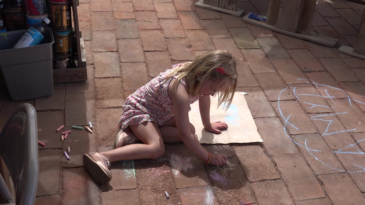 Young girl kneeling on brick patio with chalk and paper