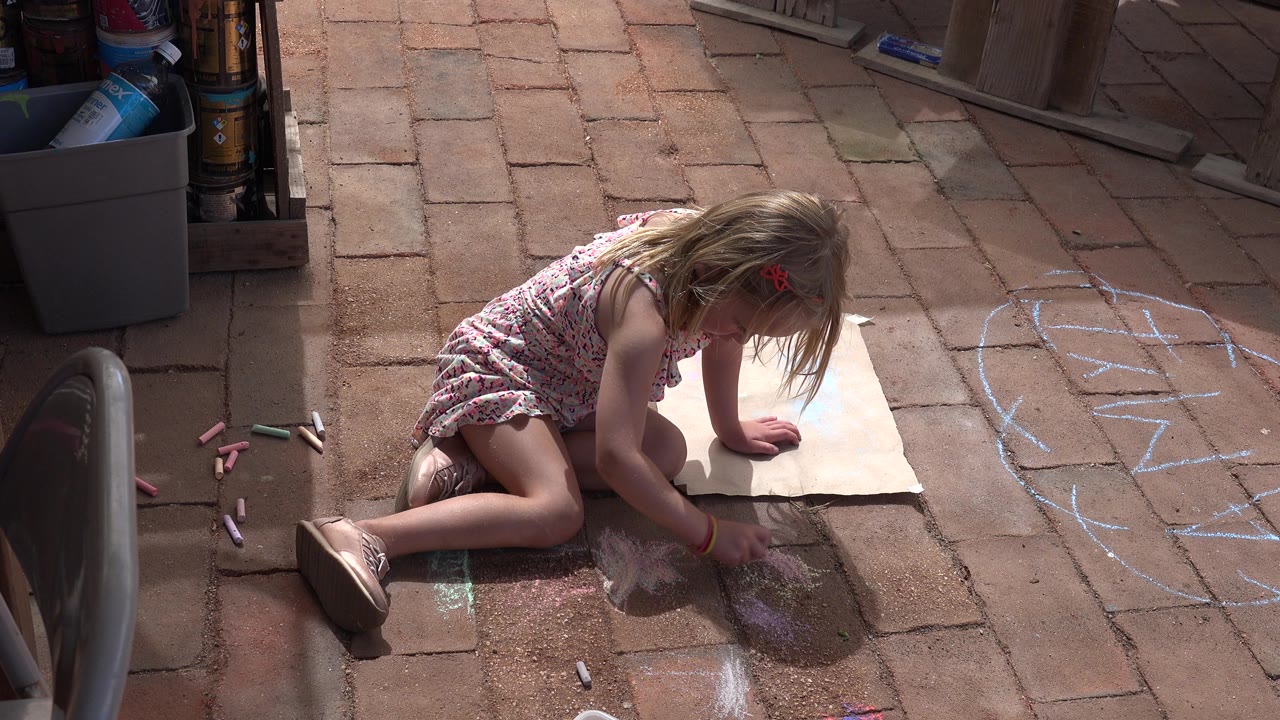 Young girl kneeling on a brick patio with chalk and paper.