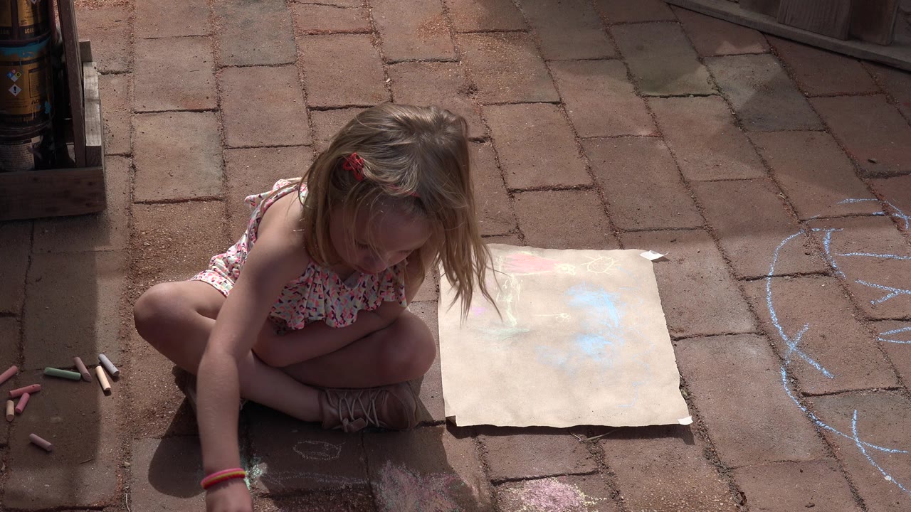 Young girl crouching beside chalk and paper on a brick sidewalk.