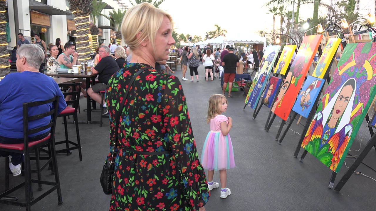Woman in a floral dress and a child beside outdoor art displays