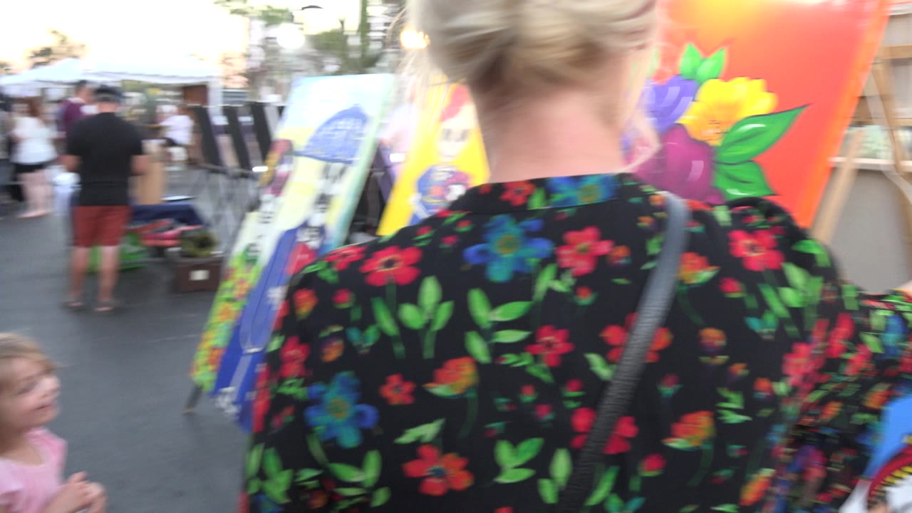 Woman and young girl walking past colorful outdoor paintings.