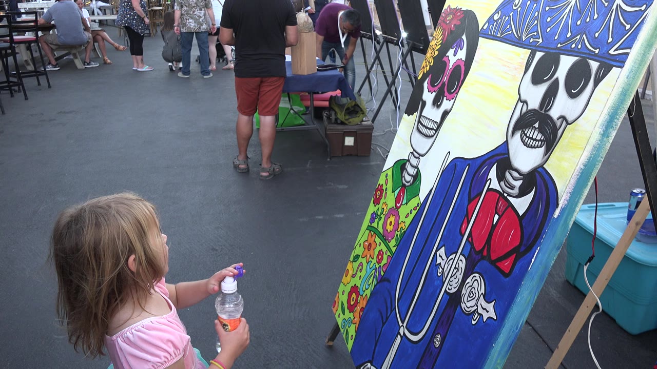 Young girl in a pink shirt looking at a colorful skeleton painting outdoors.