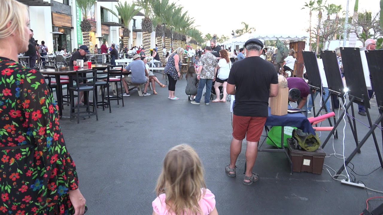 Woman and child walking past outdoor tables on a busy street.