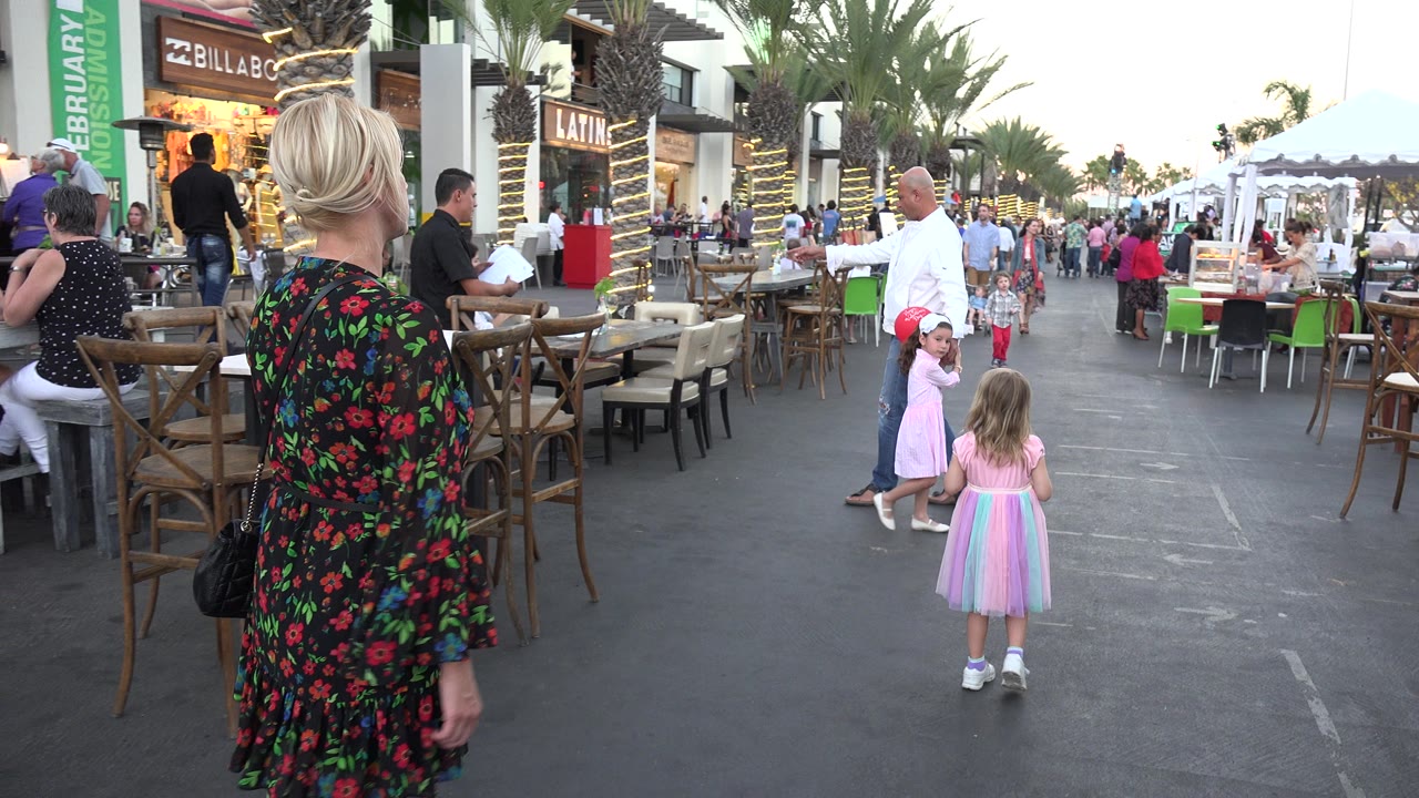 Woman walking behind a young girl on an outdoor restaurant promenade.