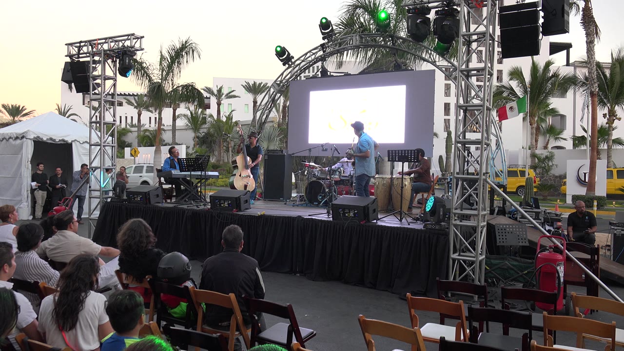 Outdoor concert stage framed by truss and palm trees.