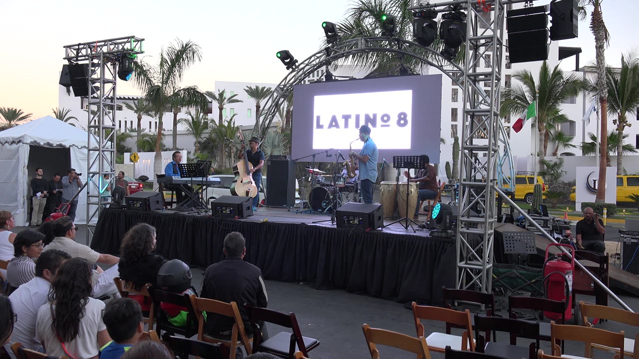 Outdoor concert stage with Latino 8 graphic and seated crowd.