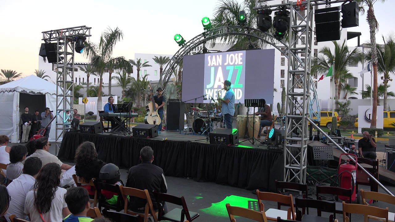 Outdoor jazz stage with audience seated in brown chairs.