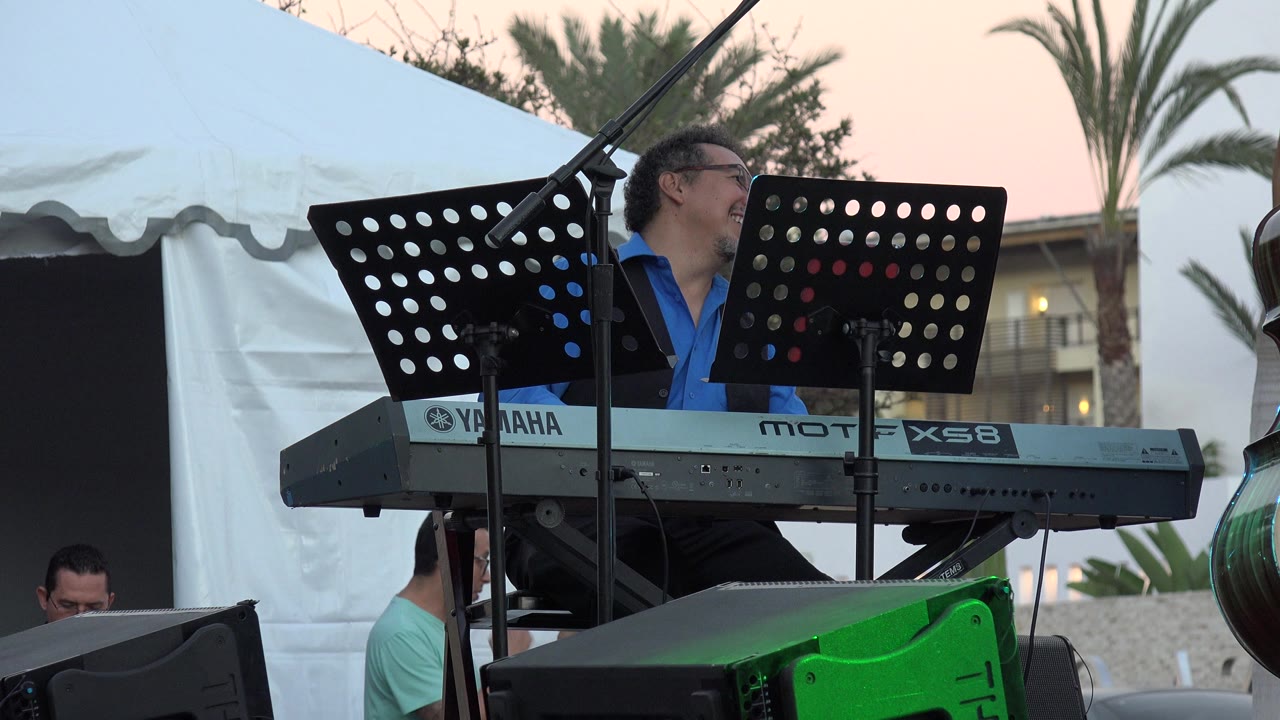 Keyboardist turned to the side behind a digital keyboard on an outdoor stage.