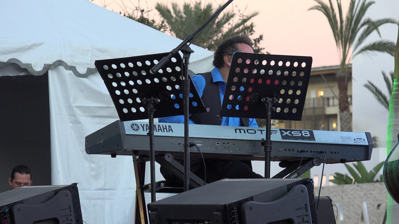 Man in blue shirt behind keyboard and music stands outdoors.