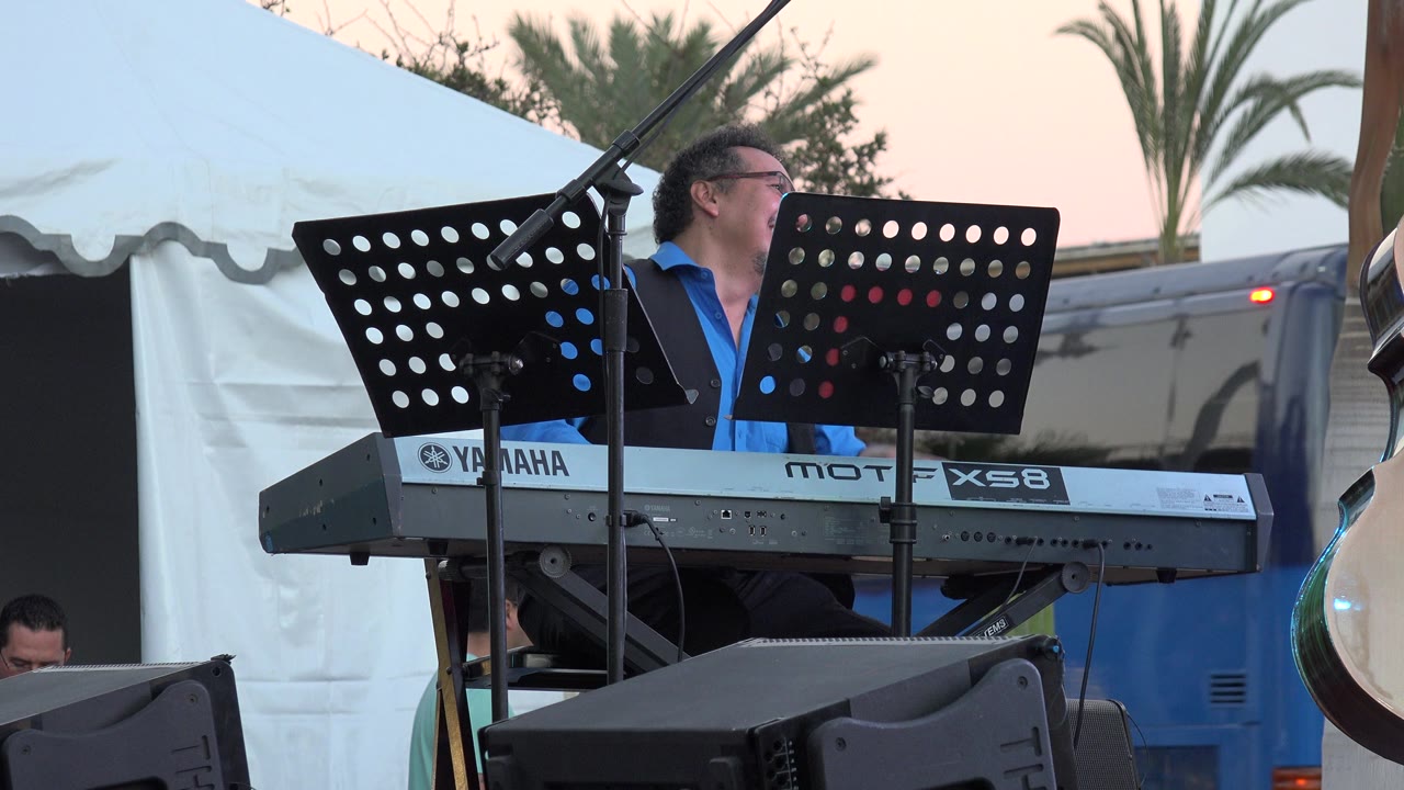 Keyboard player looking to the side with a blue vehicle behind him.