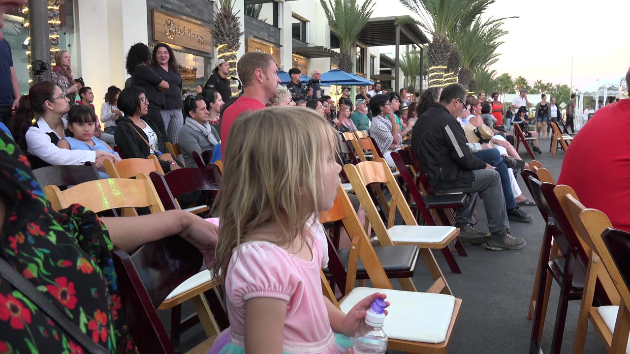 Young girl seated among folding chairs at an outdoor event.