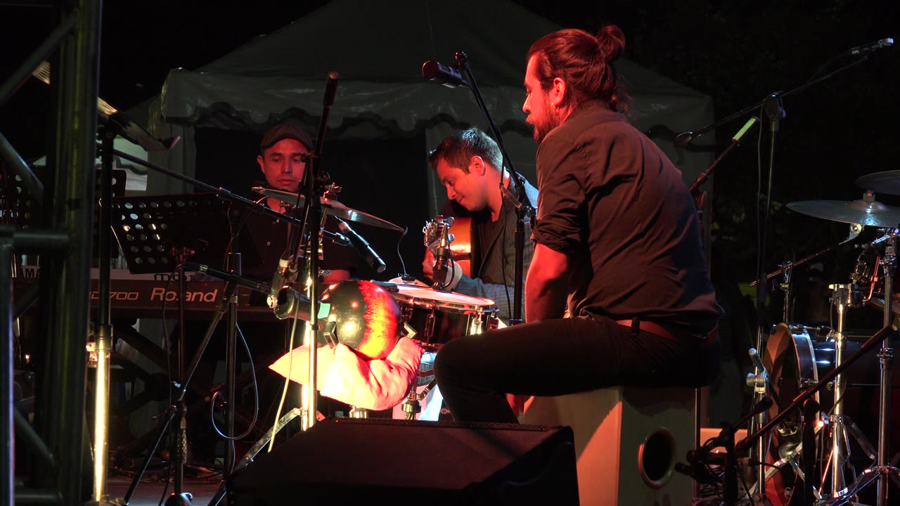 Band members onstage with a guitarist looking down near drums and microphones.