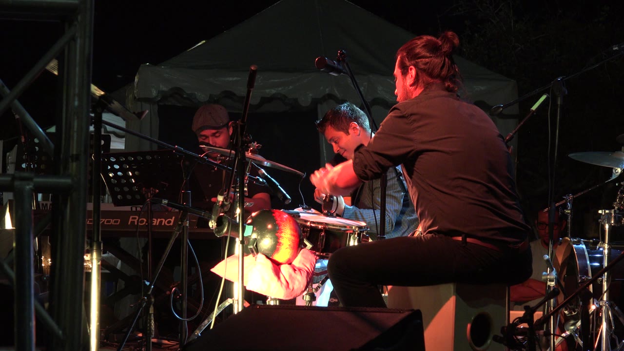 Three musicians on a dark stage with percussion and guitar.