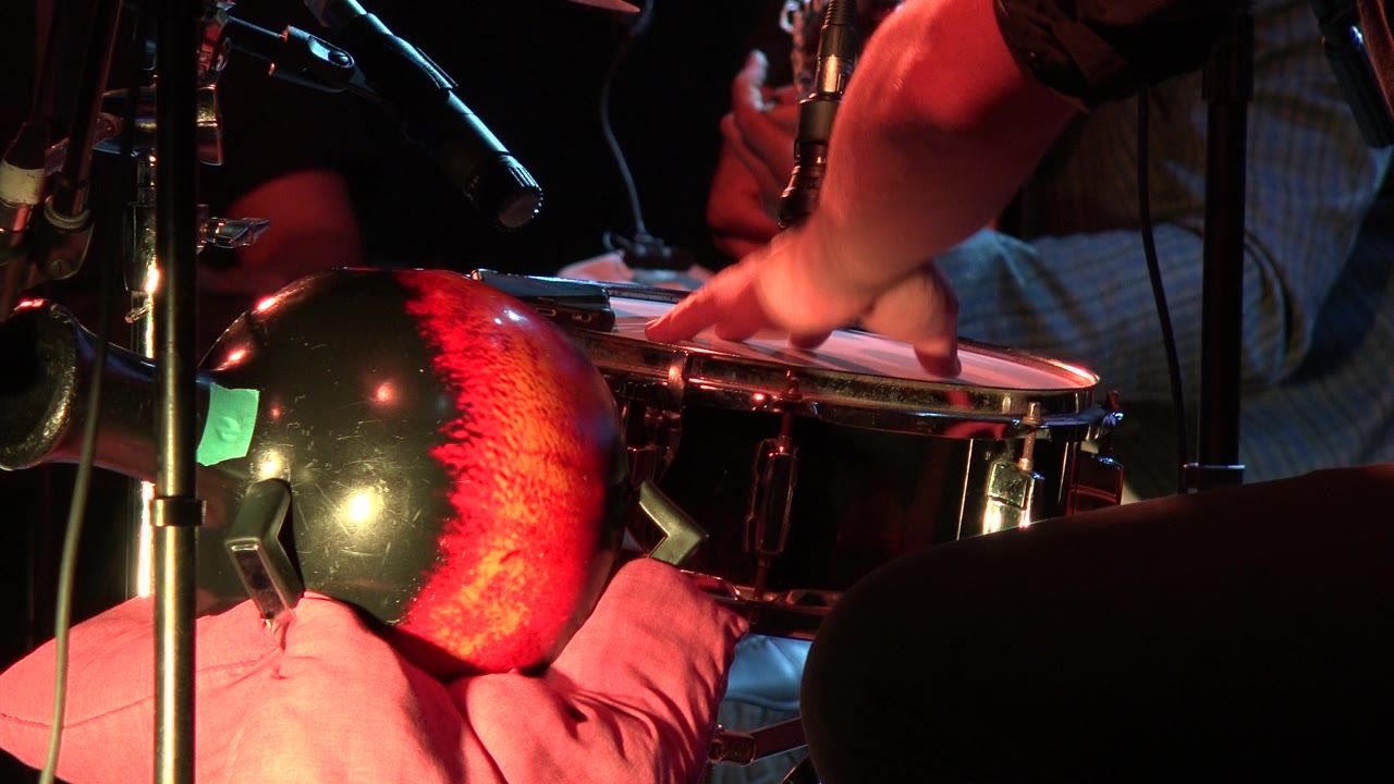 Fingers lift from a drumhead beside stage microphones.