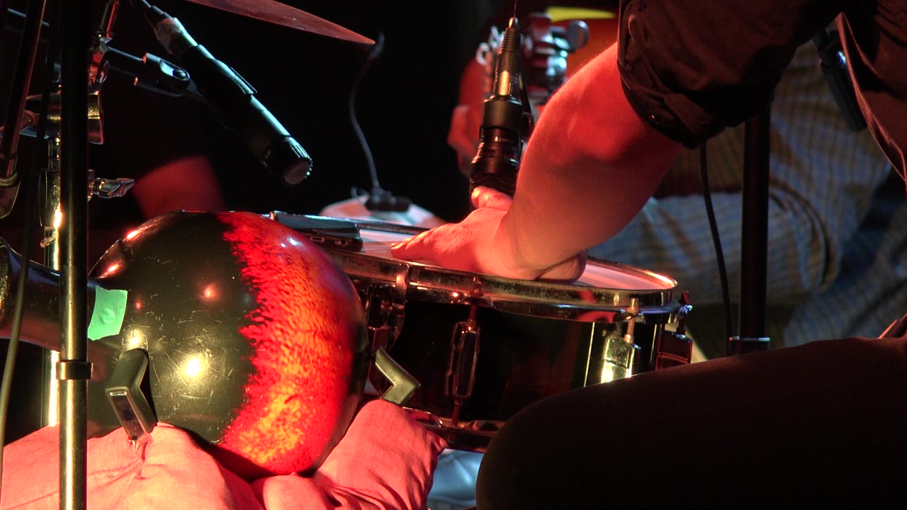 Close-up of a drummer's hand on a snare beside microphones and a red drum shell.