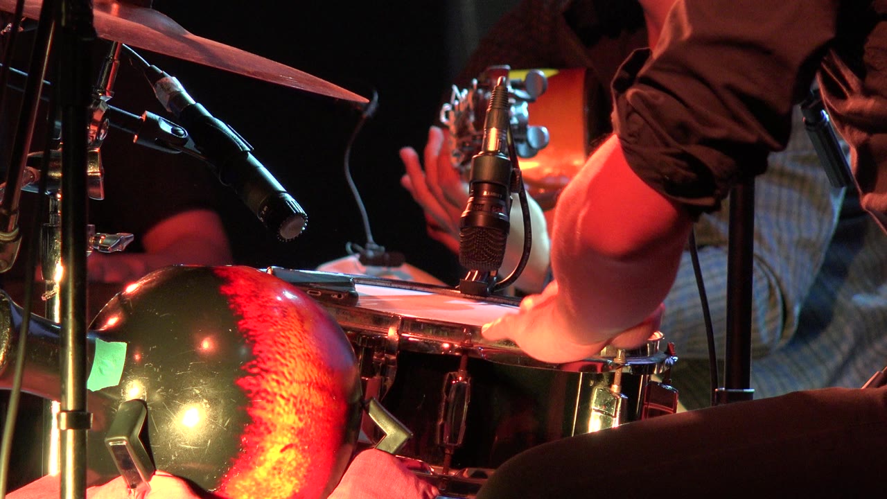 Hands playing a snare drum near microphones under red light.