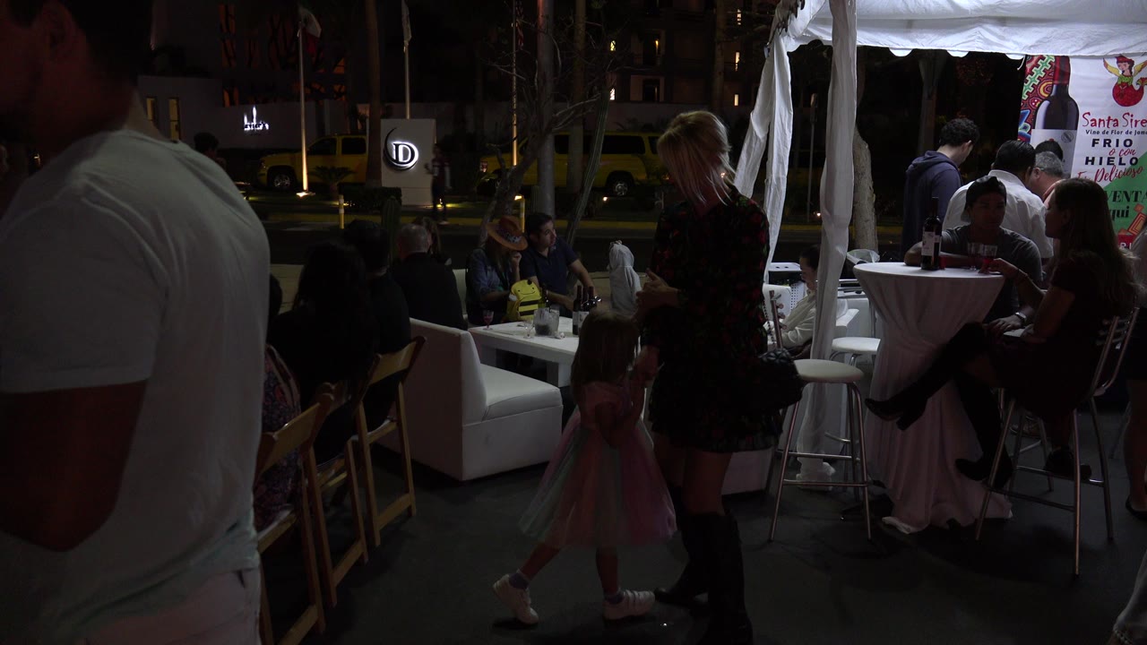 Woman and young girl dancing beside crowded restaurant seating at night.