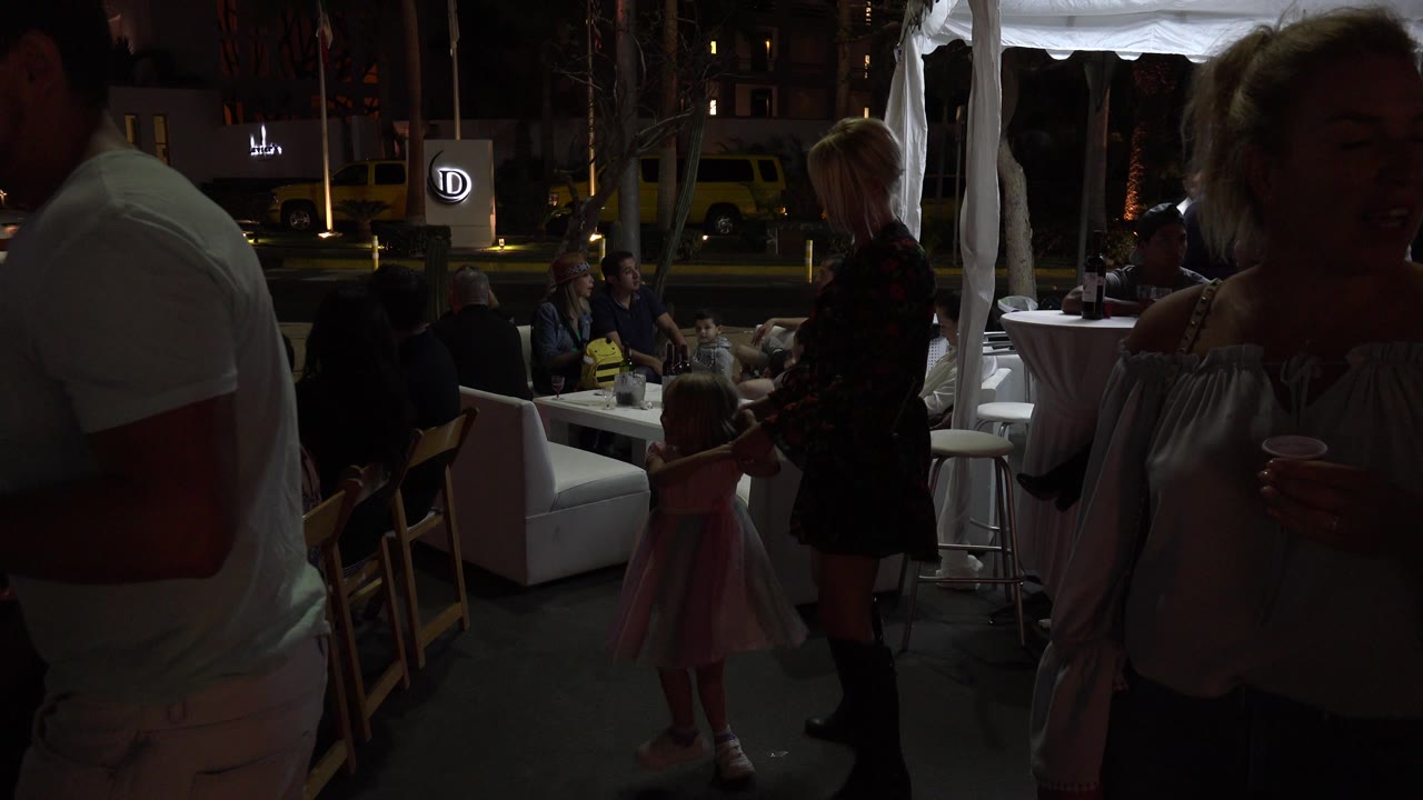 Foreground adults partly block a child near outdoor seating.