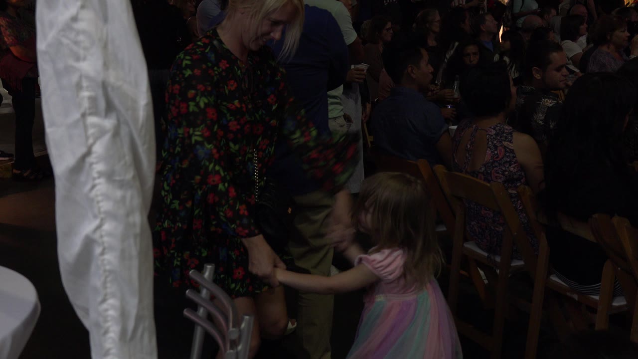 In Los Cabos, Mexico, the young girl shifts toward the adult woman while guests sit closely behind them in low event lighting.