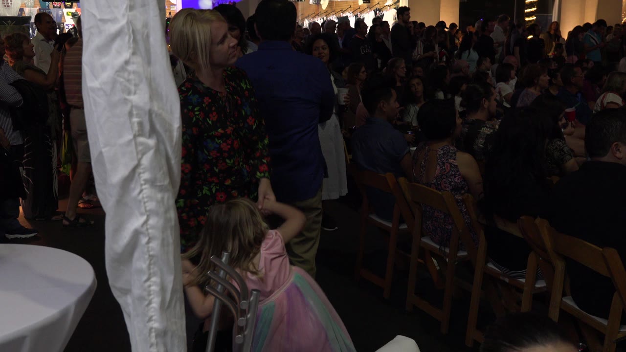 Woman and young girl at a crowded party beside a white fabric column.
