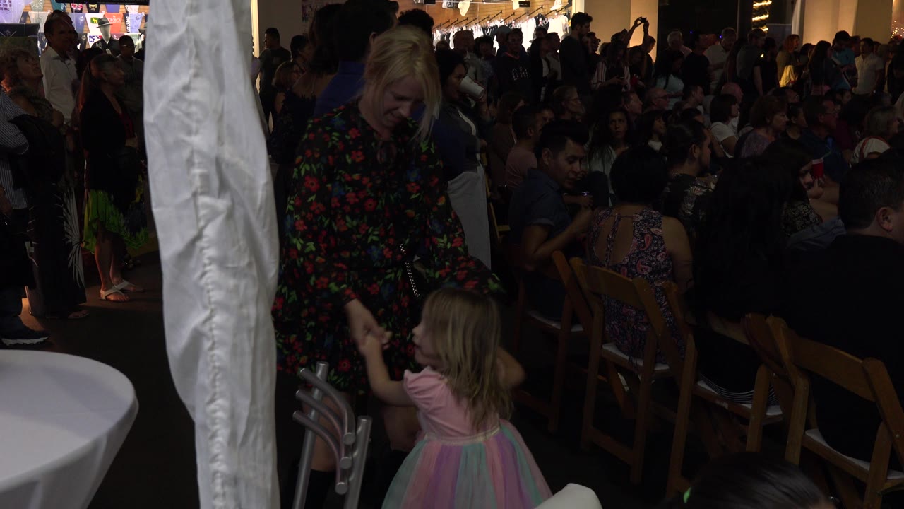 Child turns while holding the woman's hand in a crowded reception space.