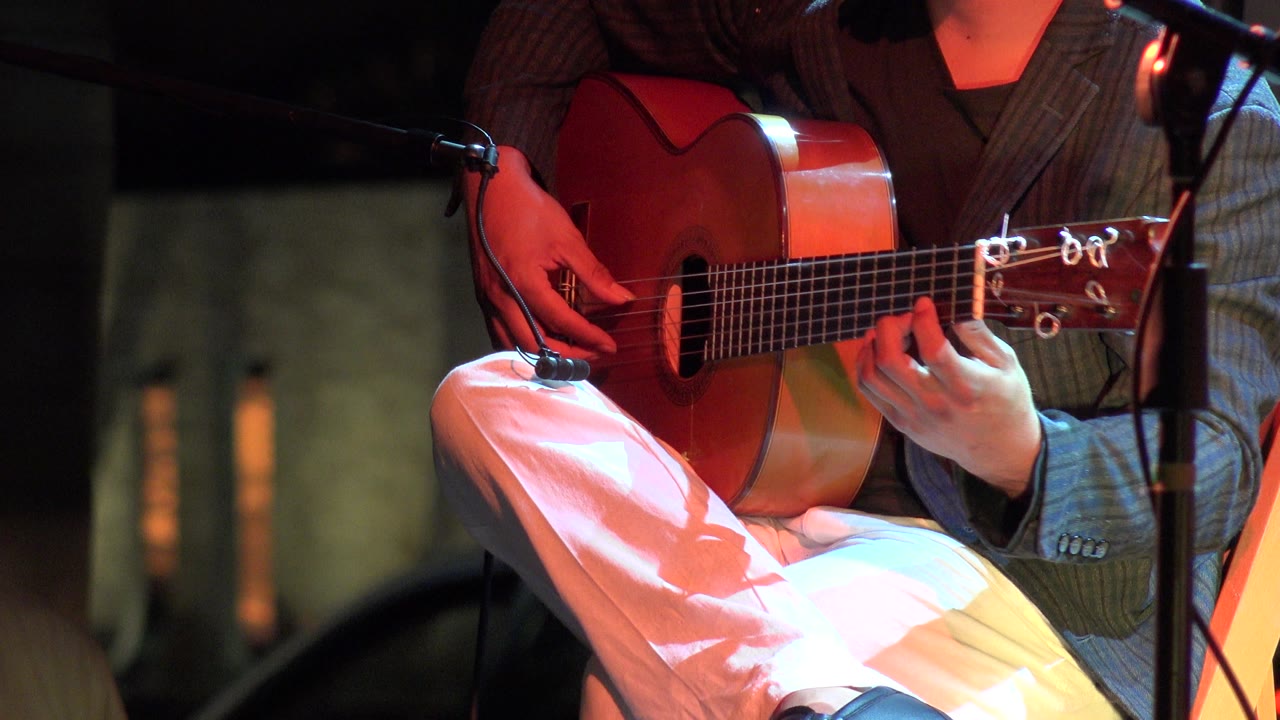 Acoustic guitar close-up with the musician's hands lit by red and cool light.