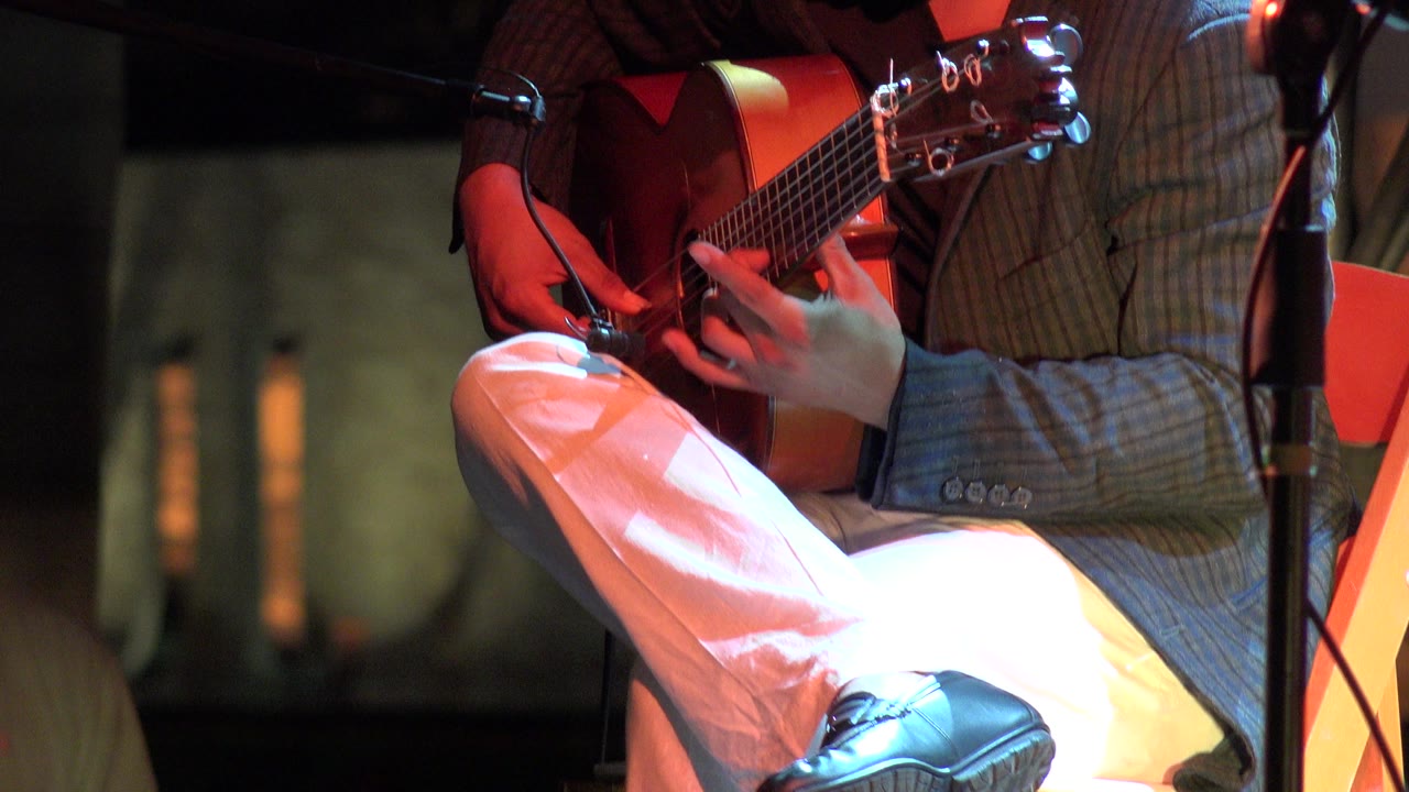 Seated guitarist playing acoustic guitar under red stage light.
