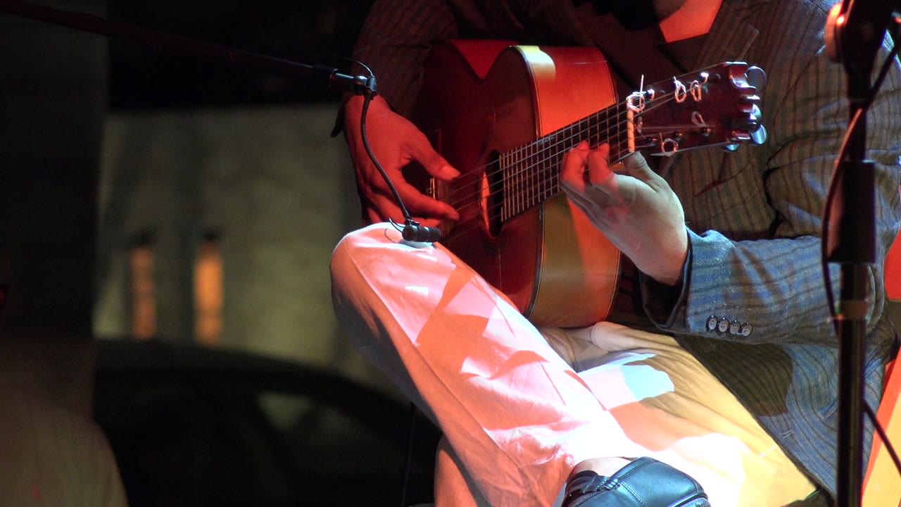 Close-up of acoustic guitar played by a suited performer.