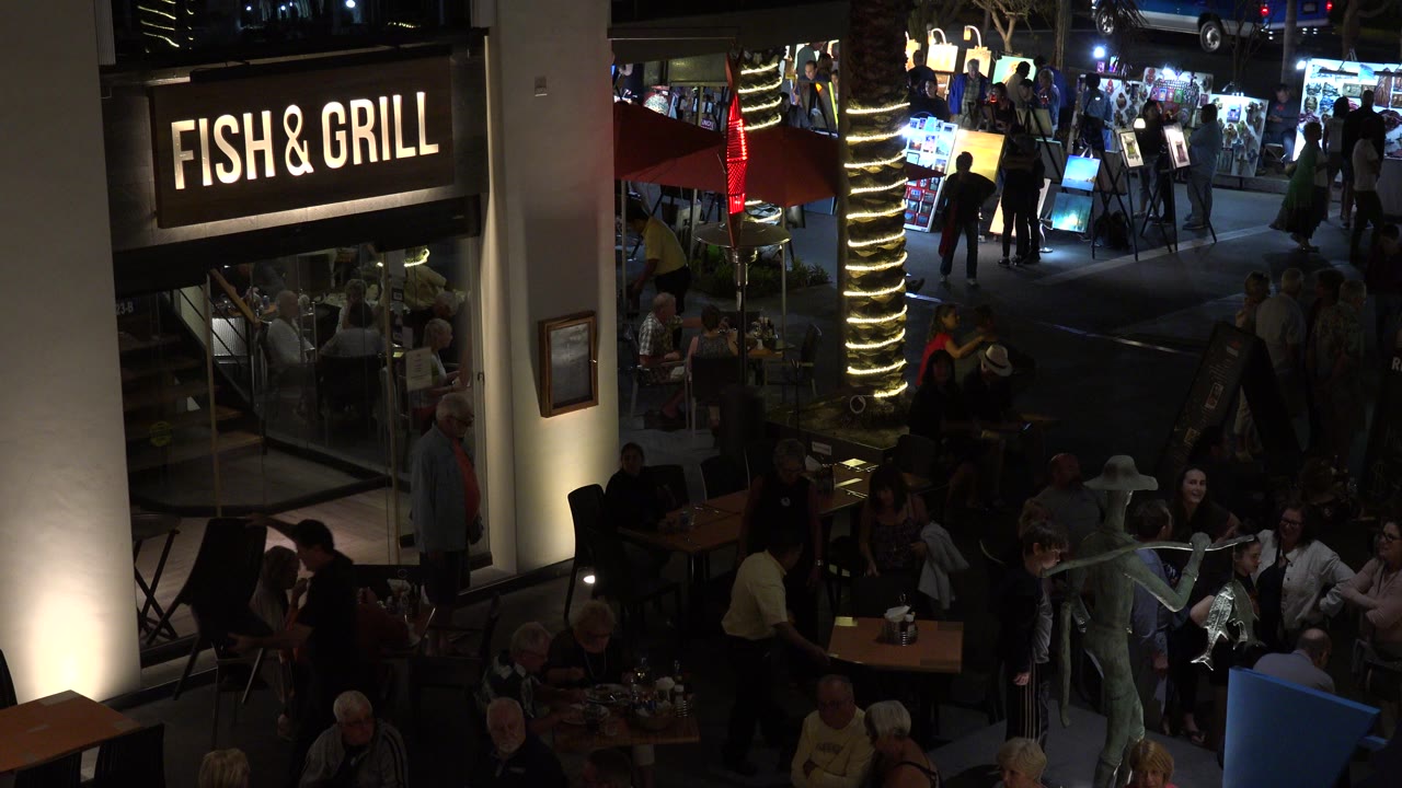 Nighttime outdoor restaurant patio with Fish & Grill sign and seated diners.