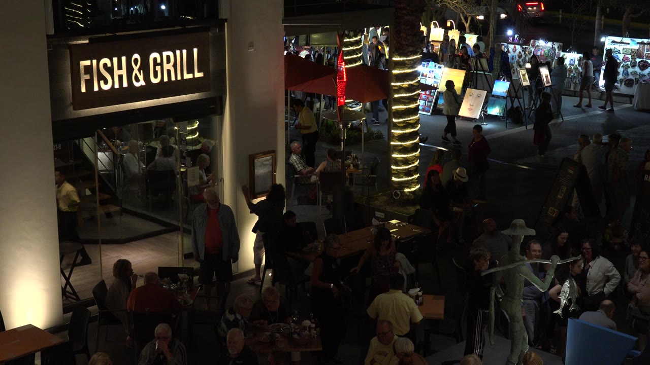 Night food court with Fish & Grill sign, diners, and pedestrians.