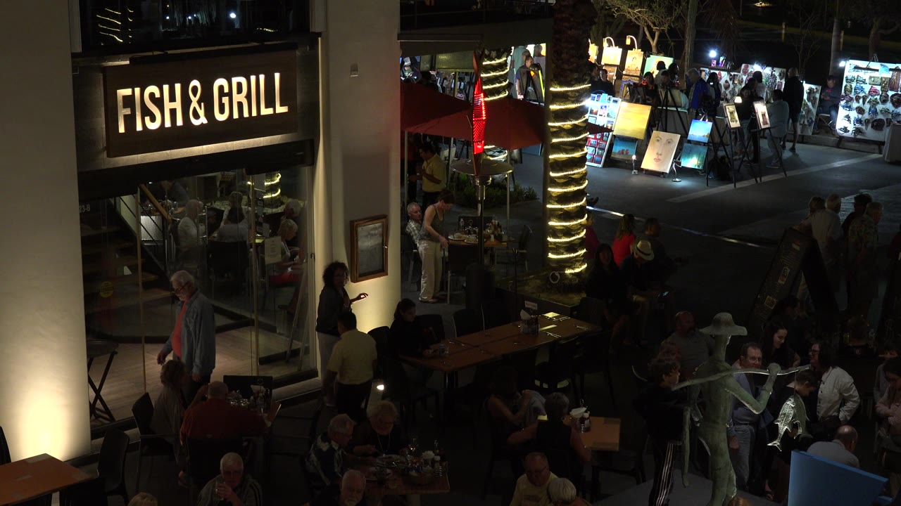 Night restaurant exterior with Fish & Grill sign, outdoor diners, and pedestrians.